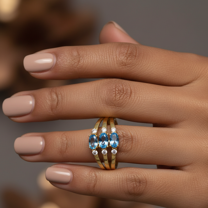 Hand wearing a gold ring with blue gemstones on a blurred background