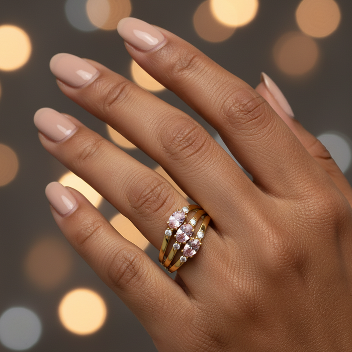 Hand wearing a gold ring with pink gemstones against a blurred lights background