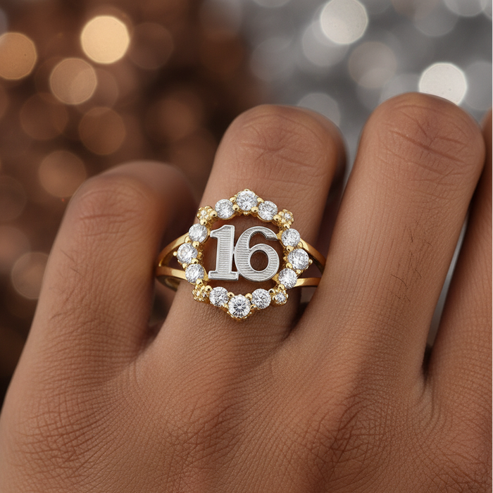 Gold ring with '16' design on a finger against a blurred background