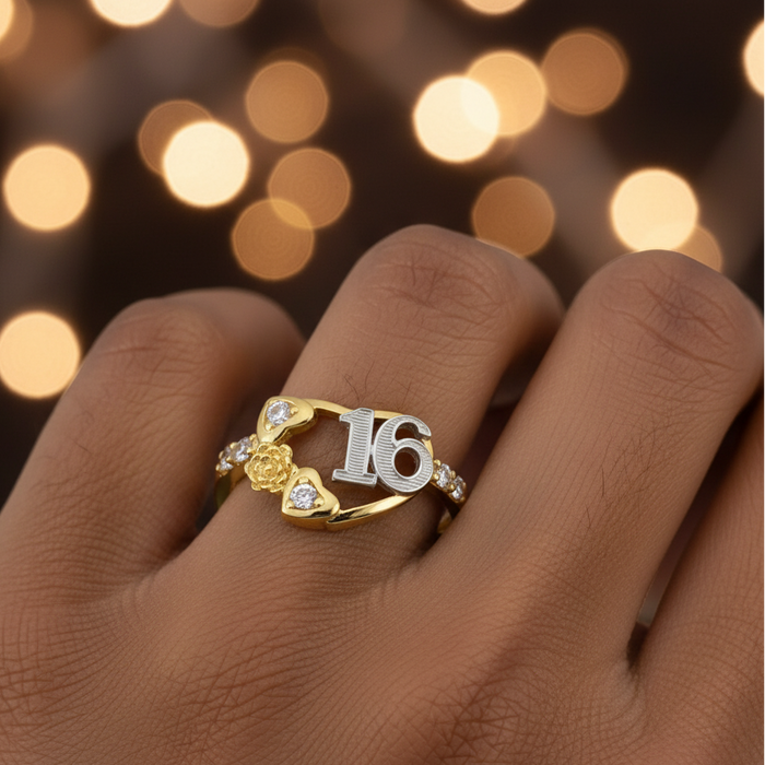 Gold and silver ring with number 16 on a hand against a blurred lights background