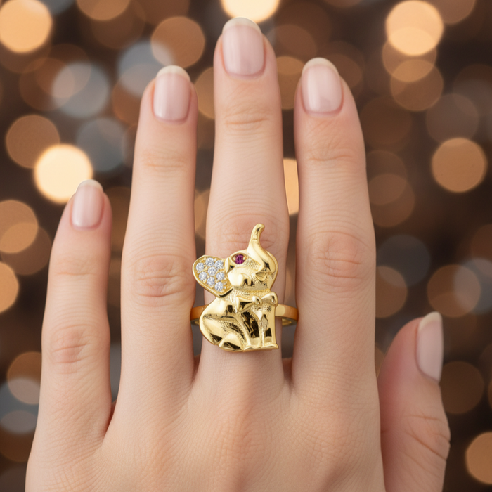 Gold elephant ring with a gemstone on a hand against a bokeh background