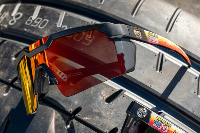 Lying on a tire is the Heat Wave Visual Future Tech Sunglasses with black frame, Hoonigan Pastrana print arms and sunblast lens.