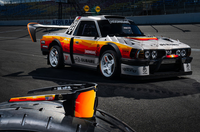 The Heat Wave Visual Future Tech Hoonigan Pastrana Sunglasses lying on tire in front of the Brataroo.