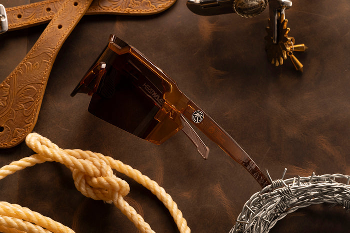 Side shot of the Future Tech Sunglasses: Saddle Z87+ on a wood table next to cowboy accessories