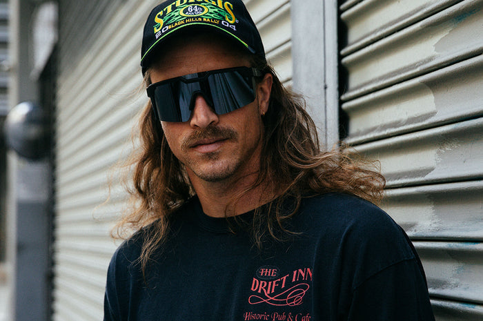 Long haired mustached man wearing Heat Wave Visual Future Tech Sunglasses with black frame and silver lens.