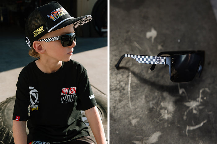 Two photo collage of a young boy wearing the Kids Lazer Face Sunglasses: Little Trouble X Heat Wave Checkered Flag with black lens outside, and a side angled shot of the glasses on a concrete floor.