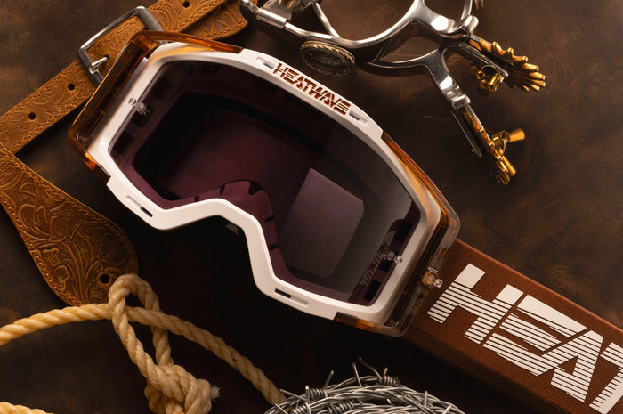 The MXG-250 Moto Goggle - Saddle on a wood table next to cowboy accessories.