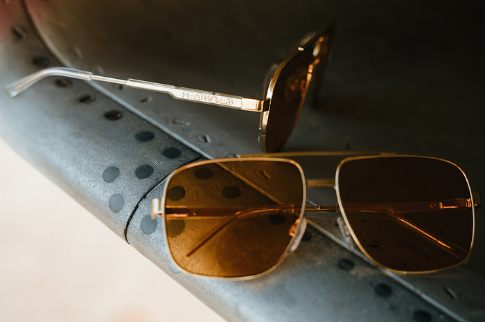 Gold-framed sunglasses with Amber lenses on a textured surface