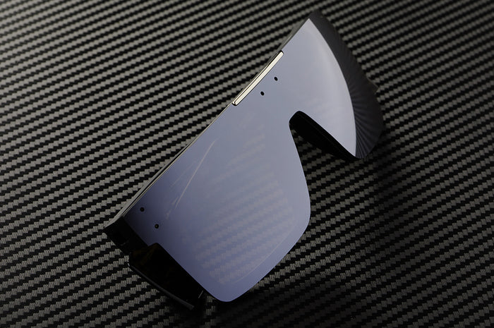 Sitting on a a table is the Heat Wave Visual Performance Quatro Sunglasses with black frame, silver lens and matching colored side shields.