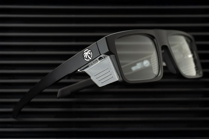 Lying on a table is the Heat Wave Visual Performance Rayth Sunglasses with black frame, anti-fog clear lenses and clear side shields.