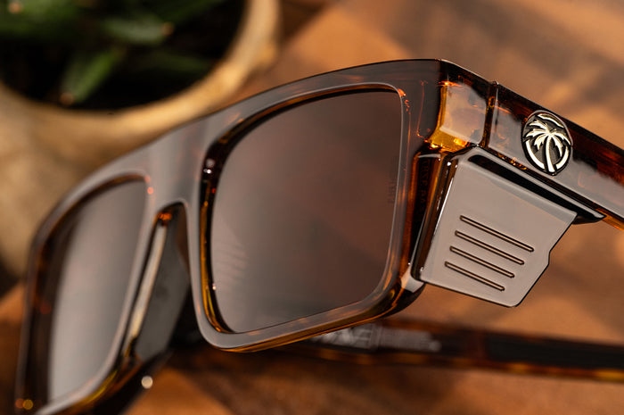 Close up shot of the Performance Rayth Sunglasses: Tortoise Z87+ with brown side shields lying on a wood table.