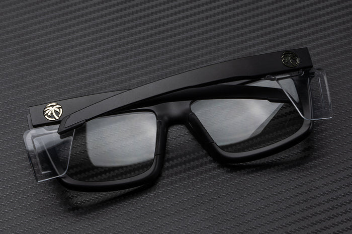 Laying on a table is the Heat Wave Visual Performance Vise Sunglasses with black frame, clear lenses and clear side shields.