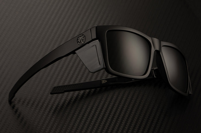 Heat Wave Visual Performance Vise Sunglasses with black frame, blacks lenses and black side shields laying on a table.