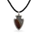 A pendant shaped like an arrowhead with  brown & gray stone in a silver frame, hung on a black leather cord. Item No. 45305