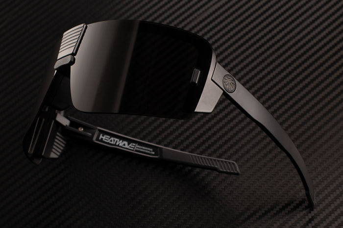 Side view of the Heat Wave Visual Vector Sunglasses with black frame and black lens on a table.