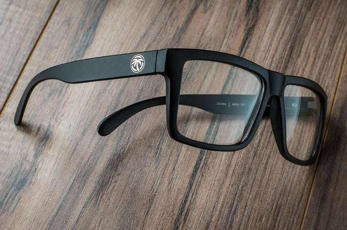 Side view of Heat Wave Visual Vise Z87 Sunglasses with black frame and clear lenses on a wooden table.