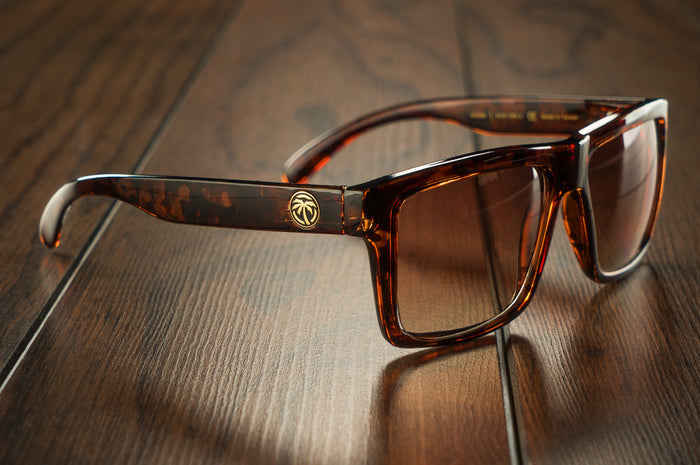 Side view of Heat Wave Visual Vise Sunglasses with tortoise frame and brown gradient lenses on a wood floor.
